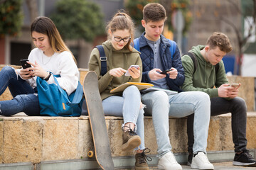 Teenage friends spending time together using smartphones outdoors