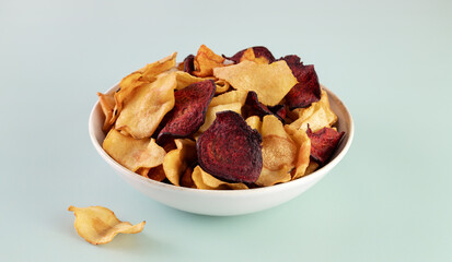A bowl of vegetable organic chips made from beets, carrots and celery root on a gray background. Top view.
