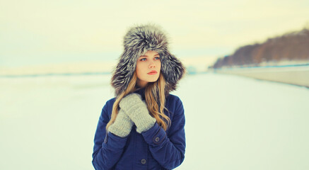 Portrait of beautiful blonde young woman posing in winter hat outdoors