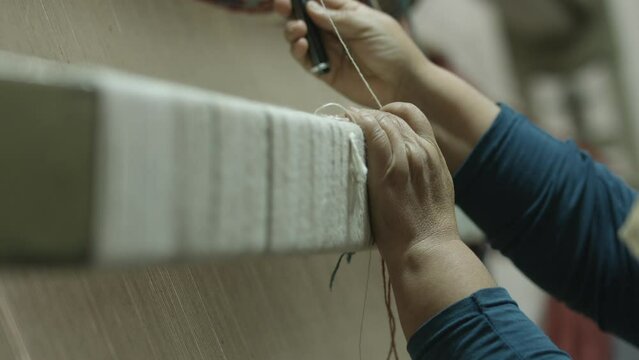A hand reaching for the threads wrapped around a carpet loom