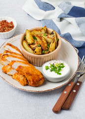 Baked golden potatoes with a crust with spices, green onions, paprika and chicken fillet on a plate.