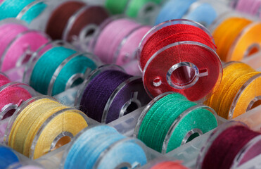 Plastic bobbins for a sewing machine with brightly colored threads in a storage box.