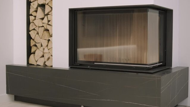 Luxurious modern design fireplace burning firewood, door with fire resistant glass window. Modern stylish fireplace and a special shelf for firewood