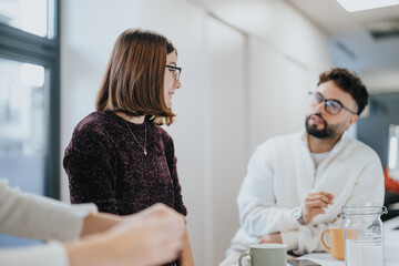 Obraz premium Cheerful businesspeople in a modern kitchen, enjoying a break and conversing over coffee and tea.