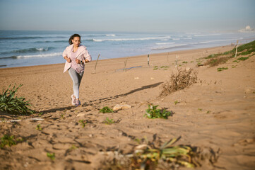 Full length portrait of an athletic woman running forward the ocean, burning calories, enjoying...