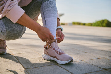 Cropped view of a sportswoman tying shoe laces, getting ready for morning run on the urban...