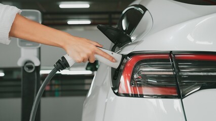 Young man travel with EV electric car to shopping center parking lot charging station in downtown...