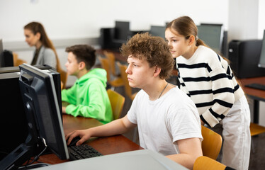 Teenagers help each other during classes in a computer class