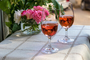 Pink wine in tasting glasses on table outside. Table is decorated with small bouquet of roses