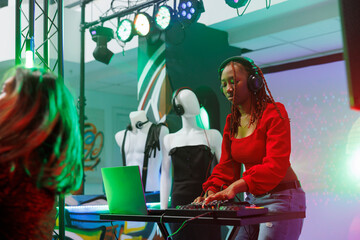 Musician using techno sounds mixer while performing on stage in nightclub. African american woman...