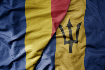 big waving national colorful flag of barbados and national flag of romania .
