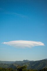 Huge lenticular cloud in blue sky in hilly landscape 