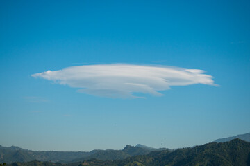Huge lenticular cloud in blue sky in hilly landscape 