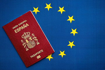 Red Spanish passport of European Union on blue flag background close up. Tourism and citizenship...