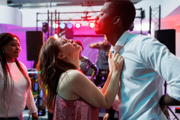 Passionate man and woman dancing and celebrating at nightlife party event. Clubbers couple making energetic moves to live music on crowded dancefloor while clubbing at discotheque