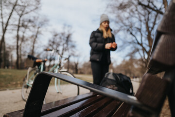 Blurred background of a woman standing in a winter park setting, focus on the empty bench in the foreground, depicting a peaceful day outdoors.