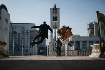 A dynamic urban scene capturing two individuals in mid-air as they leap joyfully in an outdoor setting, evoking feelings of freedom and happiness.