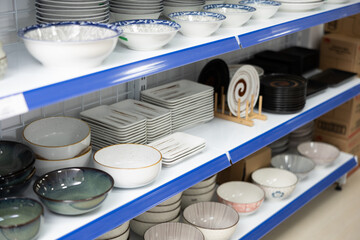 Various ceramic dinnerware, plates of different shapes and ramen bowls displayed on shelves for...