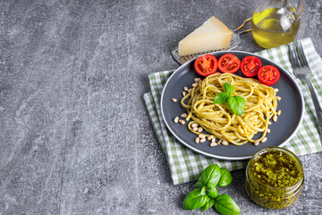 Pasta pesto, spaghetti with pesto sauce and fresh basil leaves in black plate on gray stone...