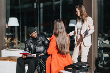 Three businesspeople engage in a discussion with documents in hand in an outdoor urban cafe setting, highlighting teamwork and partnership.