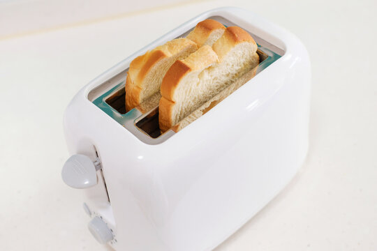 Pieces of bread in a toaster on white background, side view.