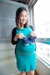 Happy smiling pragnant asian woman hold baby shoe in cozy room - 742064352