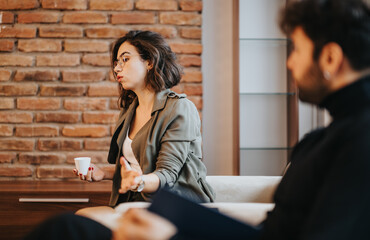 Focused young woman in conversation with male colleague in a casual office setting, expressing her...