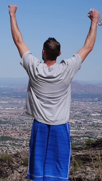 A vertical video of a young man hiking in the Arizona desert raising his hands in success. The Camelback Mountain in the distance.  	