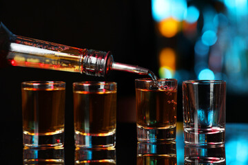 Pouring alcohol drink from bottle into shot glass at mirror bar counter, closeup