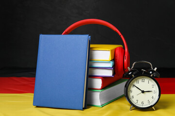 Learning foreign language. Different books, alarm clock and headphones on flag of Germany