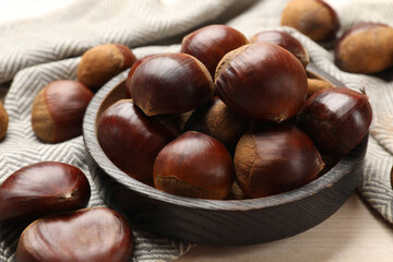 Sweet fresh edible chestnuts on light wooden table, closeup