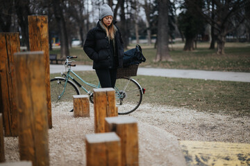 Contemplative young woman pausing by her bicycle in a chilly park.