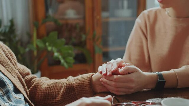 Close-up view of caring woman holding hands of elderly man and telling him supportive words at home
