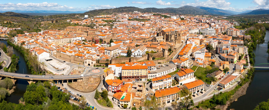 View from drone of residential area of Plasencia city with brownish tiled roofs of houses and ancient gothic roman catholic cathedral on green bank of meandering Jerte river in spring, Caceres, Spain