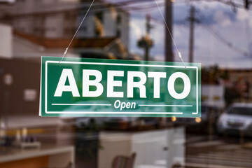 Bilingual sign with the words Aberto and Open in Portuguese and English on the glass door of a...