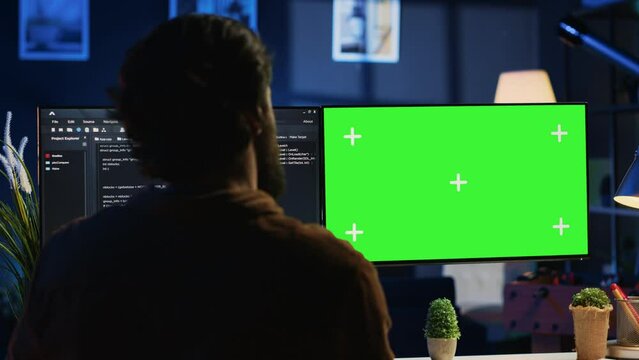 Programmer typing complex code on green screen computer in neon lit home office, developing software application. Teleworking IT specialist doing remote project tasks on mockup PC monitor, camera A