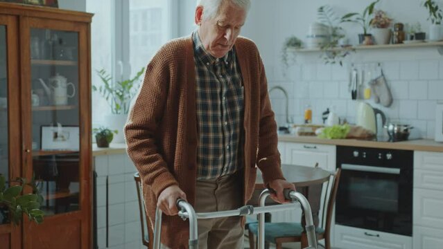 Elderly man using a walking frame to get around the house without assistance during the day. Tilt-down shot