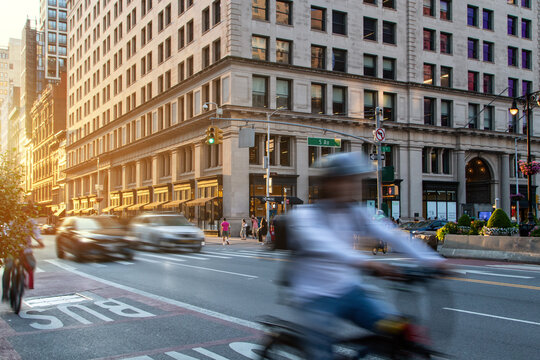 Person riding a bicycle through the busy intersection of 23rd Street and 5th Avenue in New York City with motion blur - Powered by Adobe