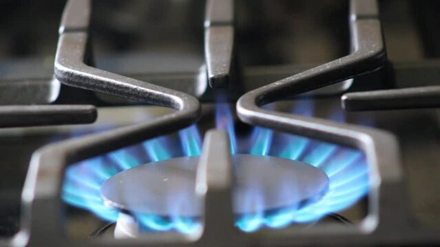 Igniting gas stove burner under metal grill to start burning blue flame