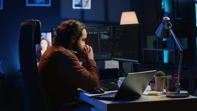 Technician focused on typing complex code in neon lit home office, developing software application. It specialist removing headphones to better concentrate on difficult task, camera A