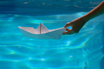 Paper boat with hand. Tourism and traveling, travel dreams vacation holiday, sailing adventure. Paper boat sailing on blue water surface.