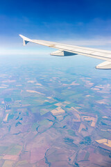 Obraz premium Aerial view from airplane window above green ground. View from the airplane window with beautiful clouds at sunrise