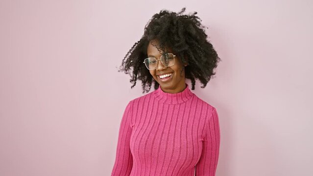 Cheerful african american woman pulls a sassy wink, her glasses glinting! standing against a vibrant pink backdrop, her joyous expression is a perfect picture of vivacity