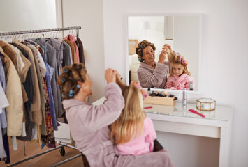 Mother, daughter and playing with hair in mirror for beauty, care and helping or getting ready. Excited mom, family and girl or kid with rollers for hairstyle, fashion and bonding together at home