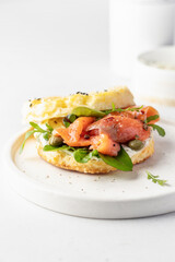 Homemade bagel sandwich with smoked salmon, cream cheese, capers and spinach for healthy breakfast on white kitchen background for breakfast