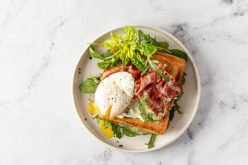 Toasts sandwich with poached egg, arugula, bacon and cream cheese on white plate marble background, top view, text space