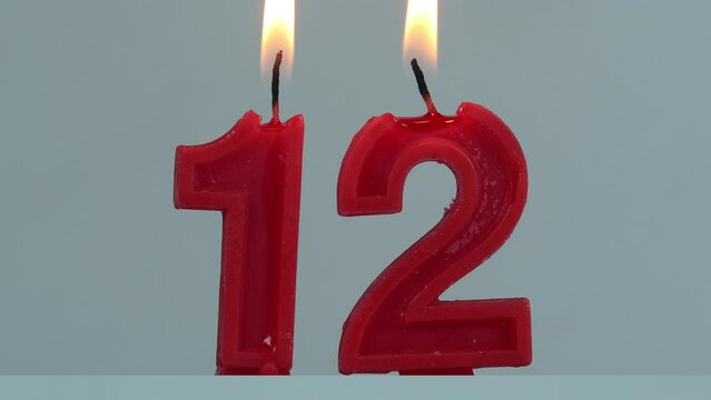 close up on timelapse melting a red number twelve birthday candle on a white background.

