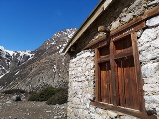 A sturdy stone building, adorned with a wooden window, nestled in front of a majestic mountain range.