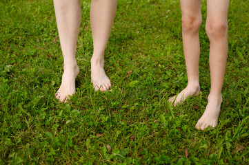 Woman and a child walk together barefoot on the grass on a lawn in a city park. The concept of a healthy lifestyle, freedom and outdoor recreation.