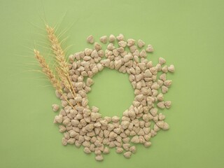 Obraz premium Extruded heart-shaped bran is poured onto a green background forming a circular void space for the text. Spikelets of wheat. The concept of proper snacking, proper nutrition and weight loss